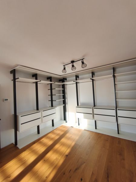 Ein Kleiderschrank im Einfamilienhaus mit Regalen, Schubladen und einem Boden in Holzoptik.