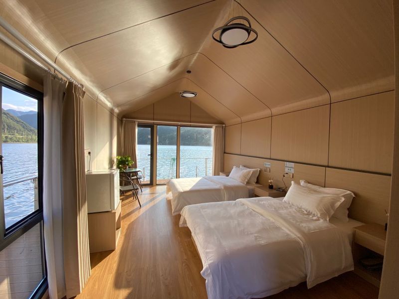 Ein Schlafzimmer in einer Hütte mit zwei Betten und einem Boden in Holzoptik, mit Blick auf den See.