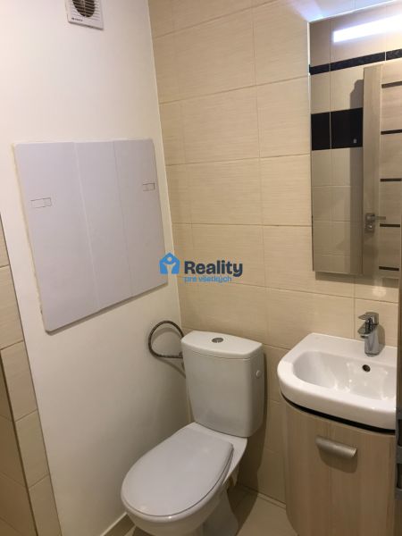 Badezimmer in einem Studio-Apartment mit Toilette und Waschbecken, helle Fliesen.