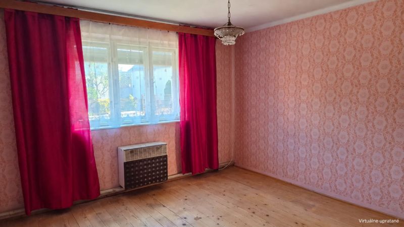 Ein Zimmer in einem Einfamilienhaus mit Tapeten, roten Vorhängen und einem Boden in Holzoptik.