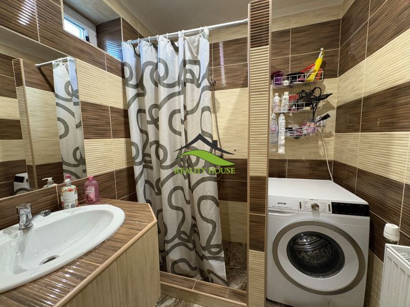 Badezimmer in einem Einfamilienhaus mit Waschbecken, Duschkabine und Waschmaschine.