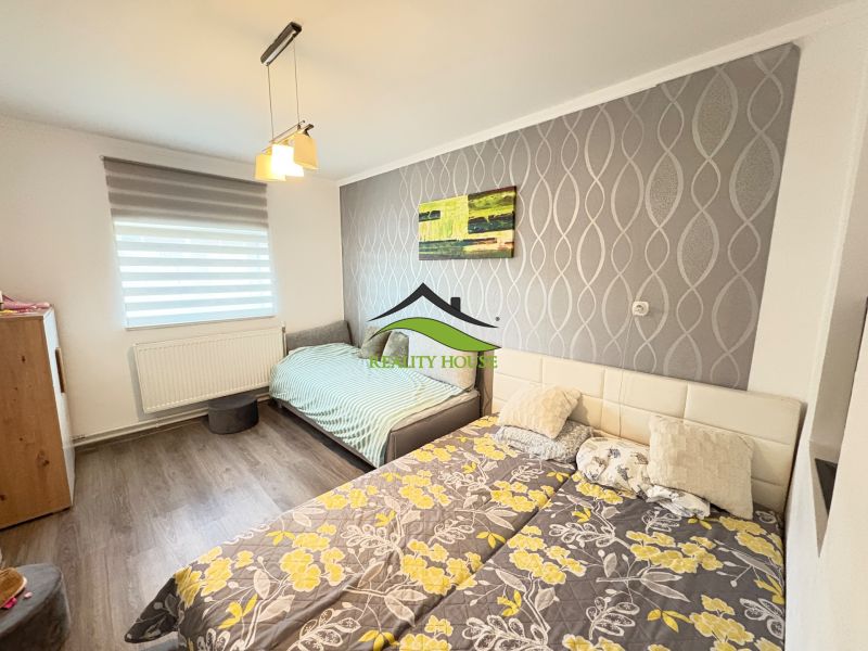 Ein Schlafzimmer in einem Einfamilienhaus mit einem Boden in Holzoptik und einer gemusterten Tapete an der Wand.