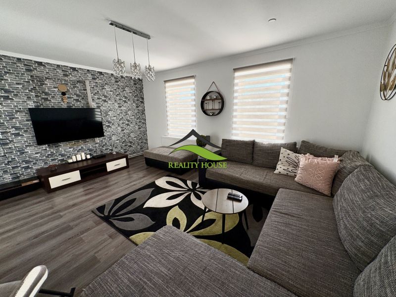 Wohnzimmer in einem Einfamilienhaus mit Holzboden, großem Sofa und gemustertem Teppich.