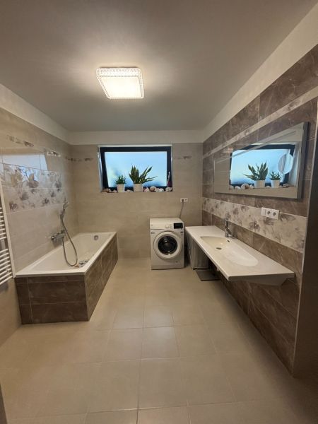Badezimmer in einem Einfamilienhaus mit Dusche, Badewanne, Waschmaschine und Spiegel auf den Fliesen.