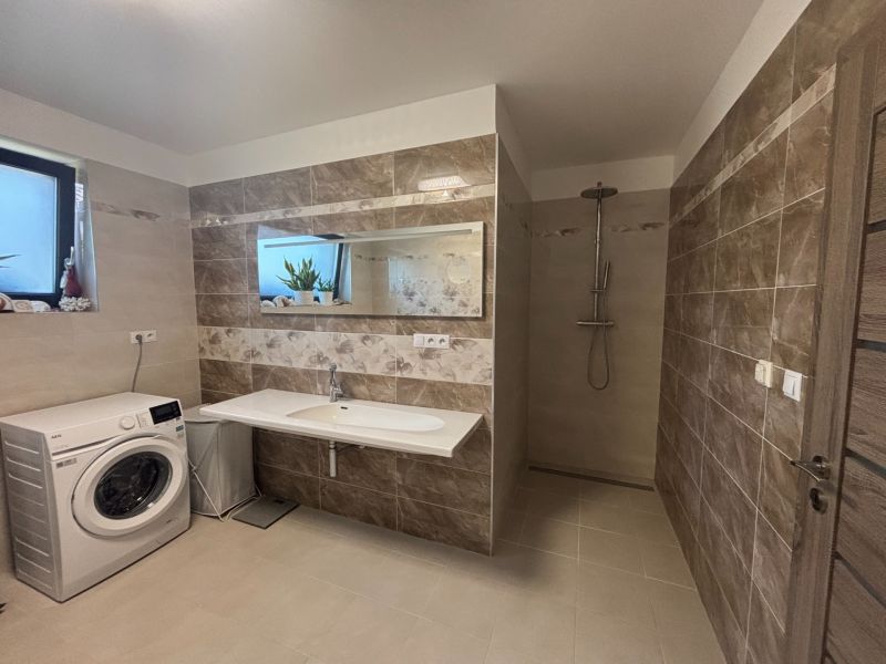 Badezimmer im Einfamilienhaus mit Waschmaschine, hellem Fliesenbelag und Duschkabine.