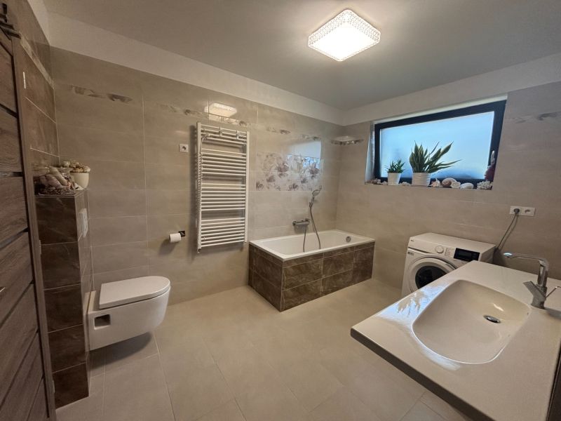 Ein Badezimmer in einem Einfamilienhaus mit Badewanne, Waschbecken und Waschmaschine in sanften Beigetönen.