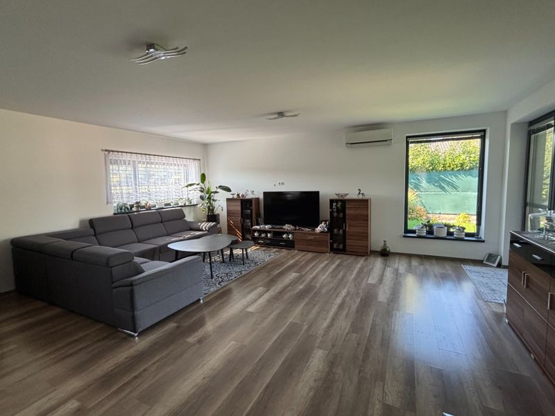 Wohnzimmer in einem Einfamilienhaus mit dunklem Sofa und Boden in Holzoptik.