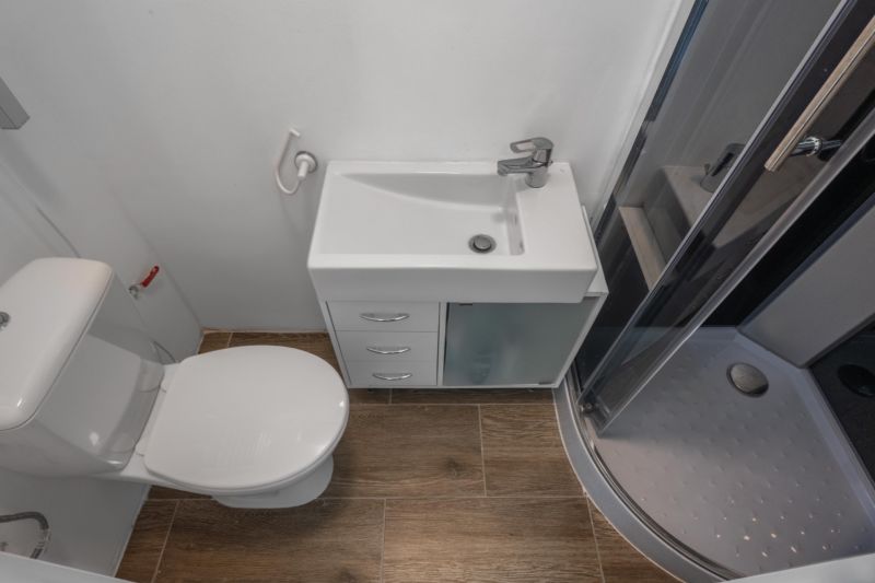 Das Badezimmer enthält eine Dusche, ein Waschbecken und eine Toilette, mit einem Boden in Holzoptik.