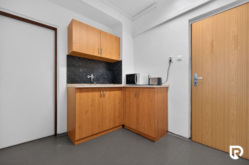Büroküche mit Schränken, Spüle, Mikrowelle und Toaster auf einem Boden mit Holzdekor.