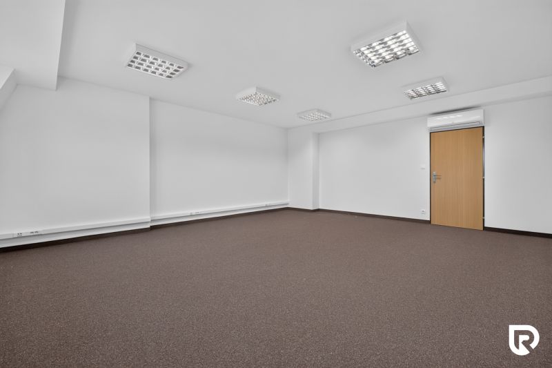 Ein leeres Büro mit braunem Teppich und weißen Wänden, der Raum ist beleuchtet und klimatisiert.