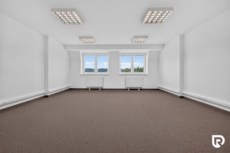 Ein geräumiges Büro mit Fenstern und Teppichboden, Beleuchtung und neutralen Wänden.