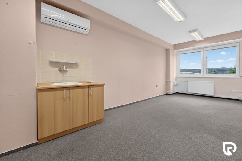 Ein Büro mit einem Waschbecken, Klimaanlage und Blick auf die Hügel; helle Wände und Teppichboden.