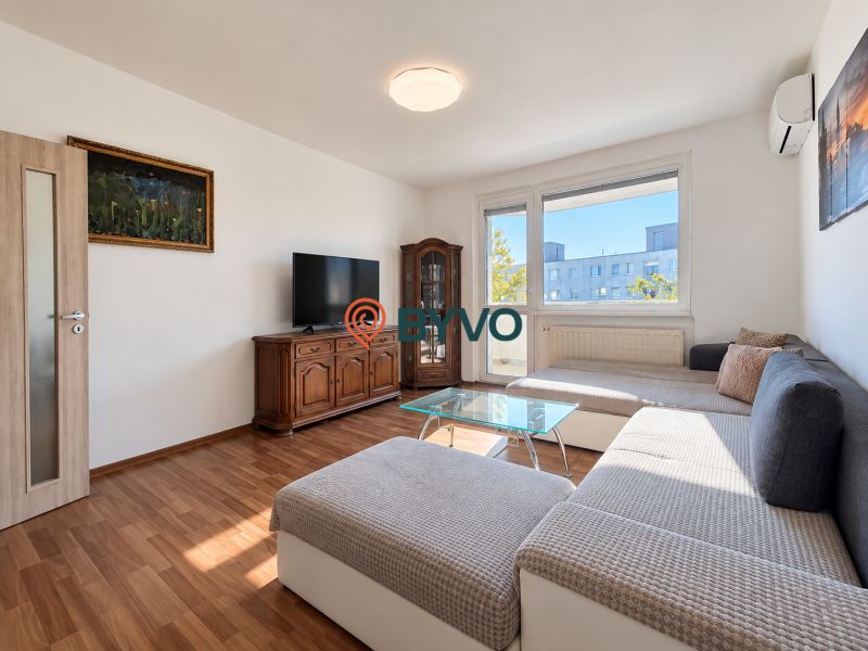 Wohnzimmer in einer Vierzimmerwohnung mit Möbeln, Holzboden und Fernseher.