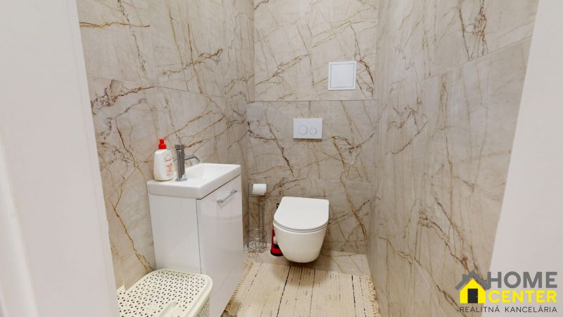 Badezimmer in einer 2-Zimmer-Wohnung mit Toilette, Waschbecken und Marmorfurnier an den Wänden.