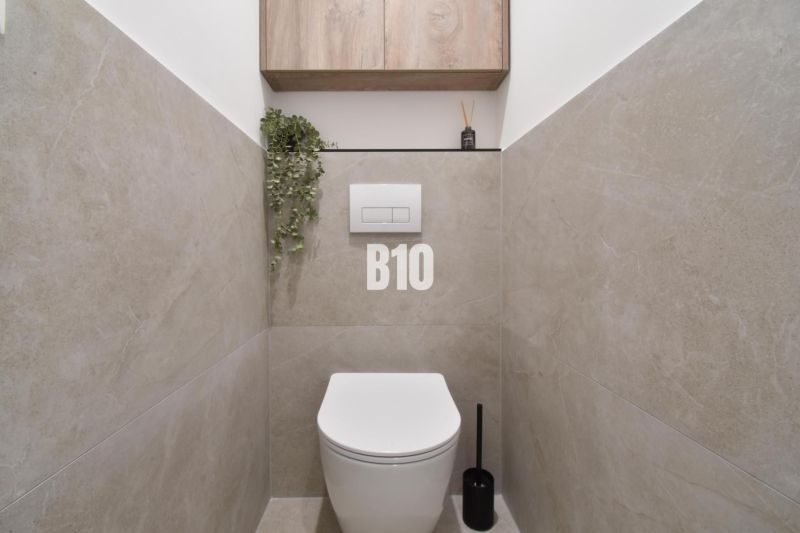 Badezimmer mit hängendem WC, Boden in Holzoptik und Stauraum.
