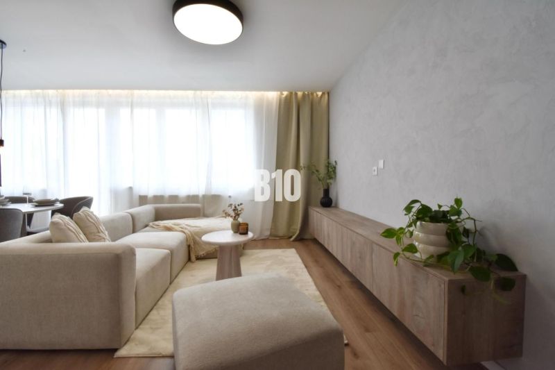 Wohnzimmer in einer 4-Zimmer-Wohnung mit Sofa, Tisch und Boden in Holzoptik.