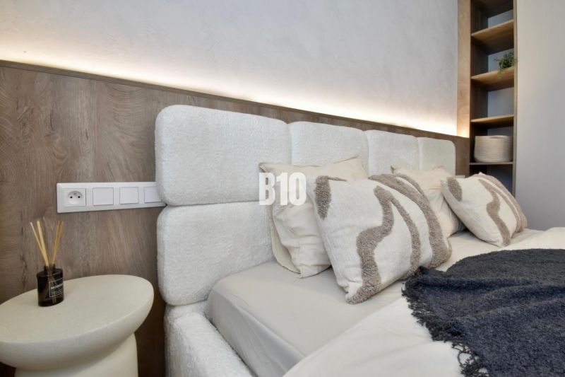 Schlafzimmer mit einem Kopfteil und Regalen in einer 4-Zimmer-Wohnung, mit sanfter Beleuchtung.