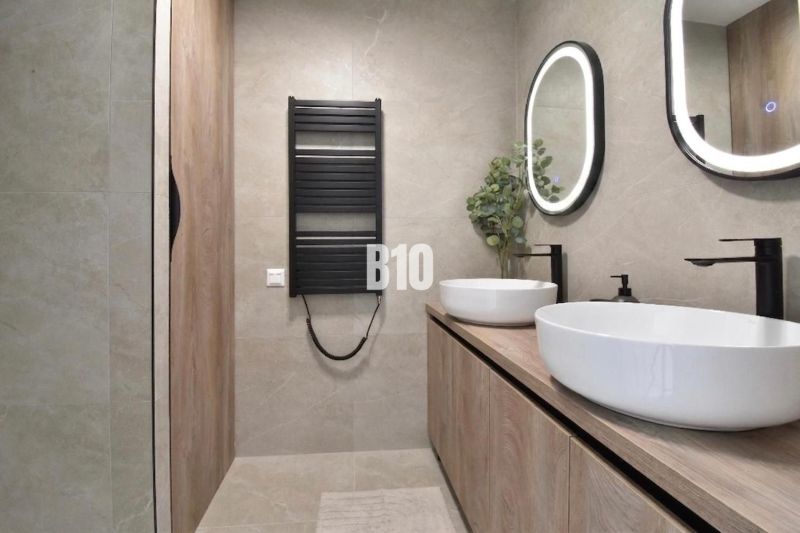 Ein Badezimmer in einer 4-Zimmer-Wohnung mit ovalen Spiegeln und Möbeln mit Holzdekor.