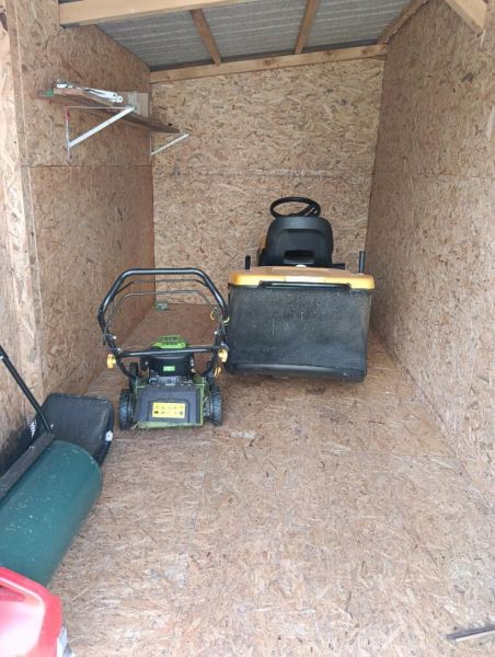 Ein Holzunterstand mit Gartentechnik, einschließlich Rasenmähern, in den Gärten.