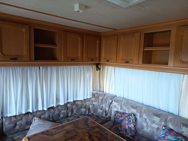 Interieur eines Wohnmobils mit Sofa, Schränken und Vorhängen, Gärten, dekorativer Tisch.