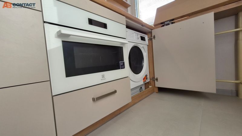 Eine eingebaute Waschmaschine und ein Backofen in der Küchenzeile einer Einzimmerwohnung mit hellem Boden.