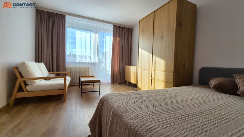 Ein Zimmer mit einem großen Fenster, einem Sofa, einem Bett, einem Schrank und einem Boden mit Holzdekor in einer Einzimmerwohnung.