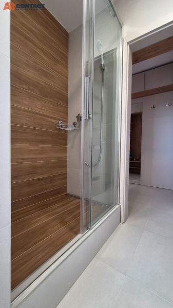Duschkabine mit Holzdekor in einer Einzimmerwohnung mit weißen Fliesen.