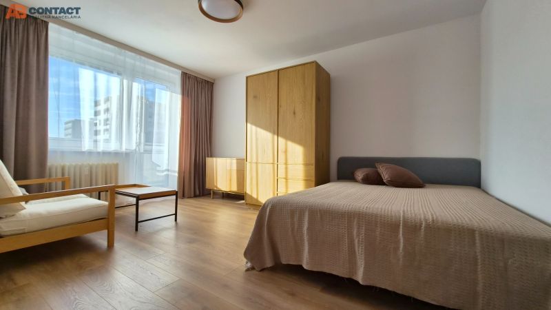 Helles Zimmer mit Bett, Sessel und Möbeln in einer Einzimmerwohnung, Boden mit Holzdekor.