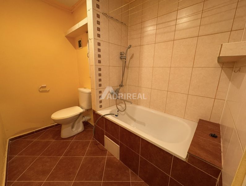 Badezimmer in einer Einzimmerwohnung mit Badewanne und Toilette mit Fliesen in Brauntönen.