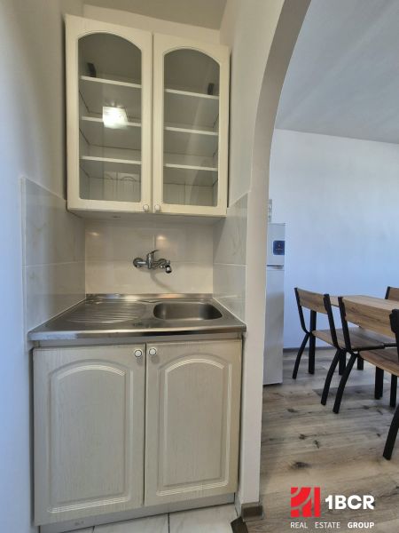 Kochnische in einem Studio-Apartment mit Spüle, Schränken und Tisch auf einem Boden mit Holzdekor.