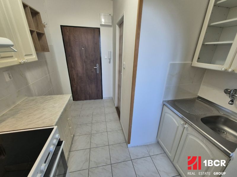 Kochnische in einem Studio-Apartment mit hellen Schränken und Geräten, Boden mit Holzdekor.