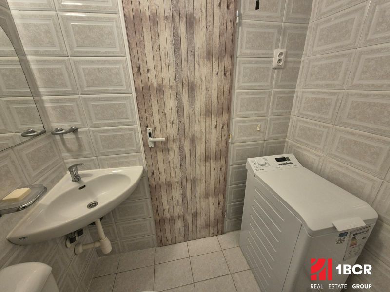 Badezimmer eines Einzimmerappartements mit Waschbecken, Waschmaschine und Fliesen aus Keramikfliesen.