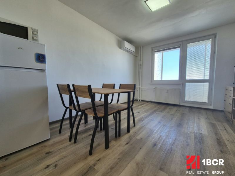 Einzimmerwohnung mit Kühlschrank, Holzboden und Esstisch mit Stühlen.