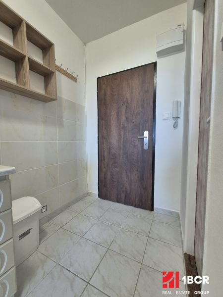 Eine Einzimmerwohnung mit Fliesenboden, einem Holzregal und einer Tür mit Holzdekor.