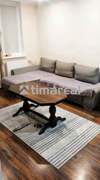 Wohnzimmer einer 3-Zimmer-Wohnung mit Sofa, Tisch, Holzboden und Teppich.
