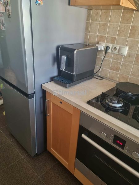 Küche in einer 3-Zimmer-Wohnung mit Kühlschrank, Herd und Kaffeemaschine auf einer Steinarbeitsplatte.