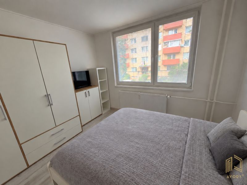 Helles Schlafzimmer in einer 2-Zimmer-Wohnung mit großem Bett, weißem Kleiderschrank und Fernseher.