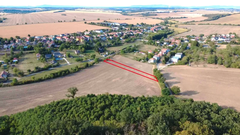 Luftaufnahme von landwirtschaftlichen und forstwirtschaftlichen Flächen in Podhájska, mit dem Dorf im Hintergrund.