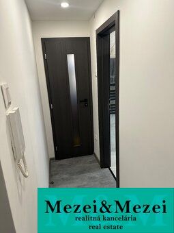 Der Flur in einer 2-Zimmer-Wohnung mit dunklen Türen und einer Gegensprechanlage an der Wand.