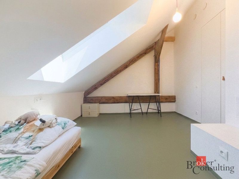 Dachzimmer mit Bett, Holzboden und Dachfenster in einer 3-Zimmer-Wohnung.
