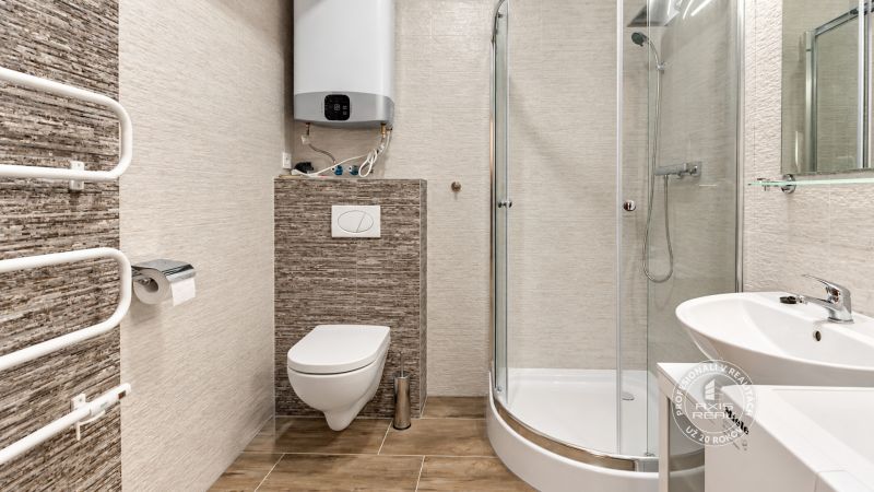 Badezimmer in einer 2-Zimmer-Wohnung, Duschkabine, Waschbecken und Toilette mit Holzdekor am Boden.