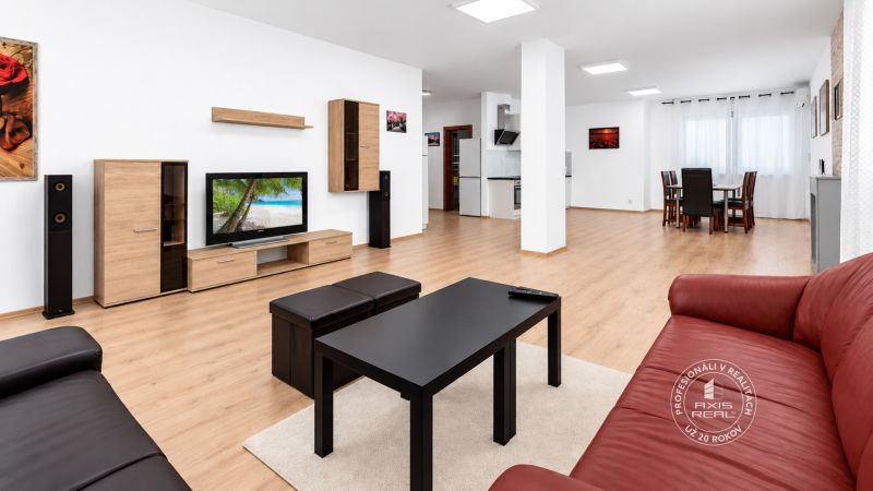 Ein geräumiges Wohnzimmer mit einem roten Sofa, einem Fernseher und einem Boden in Holzoptik.