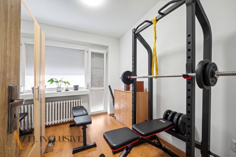 Fitnessstudio im Einfamilienhaus mit Bank, Hanteln und Boden in Holzoptik.