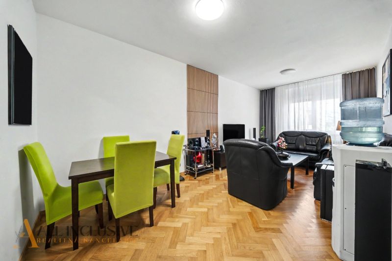 Wohnzimmer mit schwarzen Sofas, Esstisch und Holzboden.
