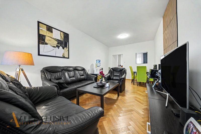 Wohnzimmer in einem Einfamilienhaus mit schwarzen Ledermöbeln und einem Boden in Holzoptik.
