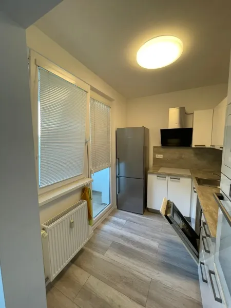 Küche in einer 2-Zimmer-Wohnung mit Holzboden, weißen Schränken und eingebautem Gerät.