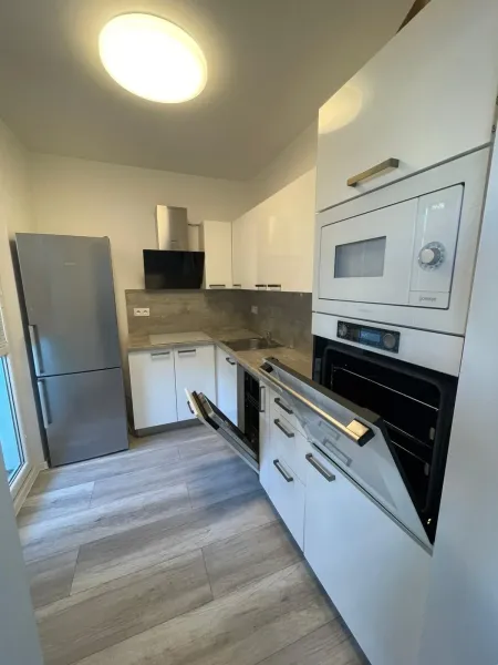 Küche mit eingebautem Backofen, weißen Schränken und Holzboden in einer Zweizimmerwohnung.