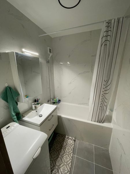 Badezimmer in einer 2-Zimmer-Wohnung mit Badewanne, Waschbecken, Waschmaschine und Fliesen.