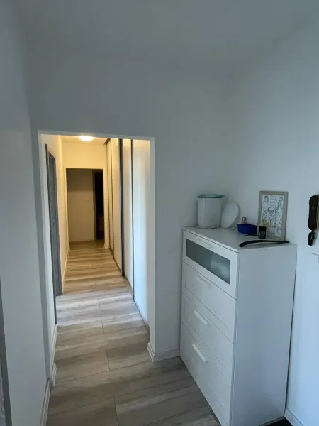 Der Flur in einer 2-Zimmer-Wohnung mit einer weißen Kommode und einem Boden in Holzoptik.