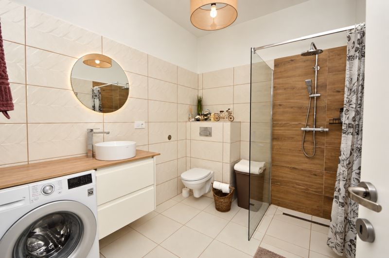 Badezimmer mit Waschmaschine, Duschkabine und Boden mit Holzdekor in einer Einzimmerwohnung.